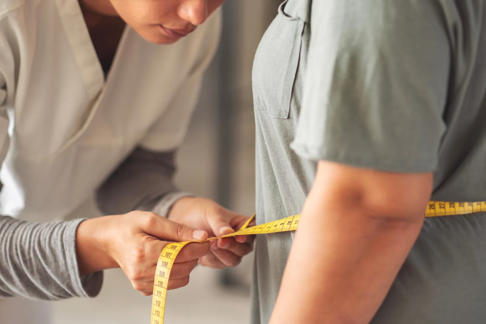 A nutritionist measures a woman's body with a tape measure.