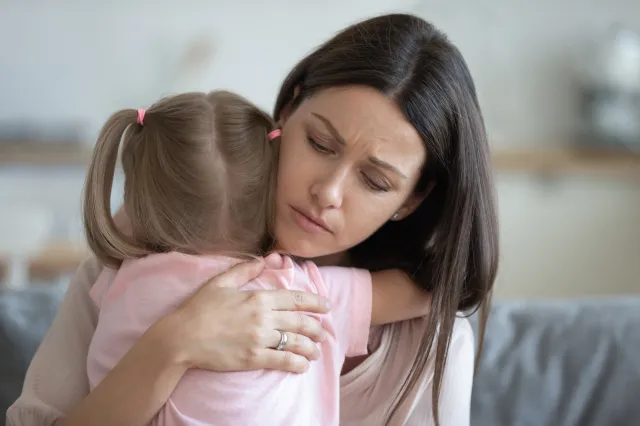 Woman looking worried while hugging young girl.