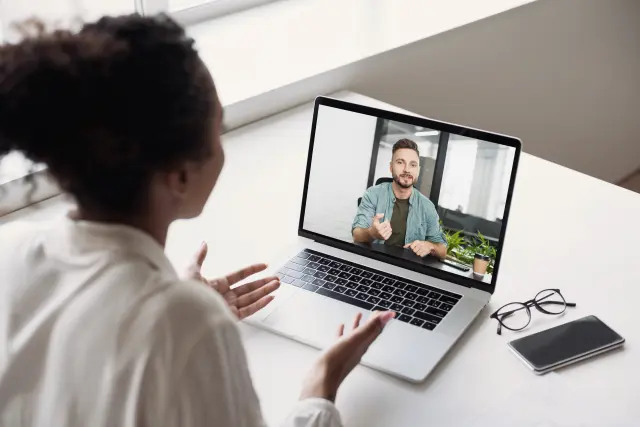 Woman on a video call with a man on a laptop screen in an office setting.