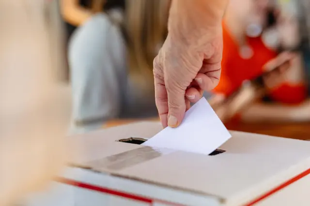 Close-up of hand placing ballot into voting box at election.