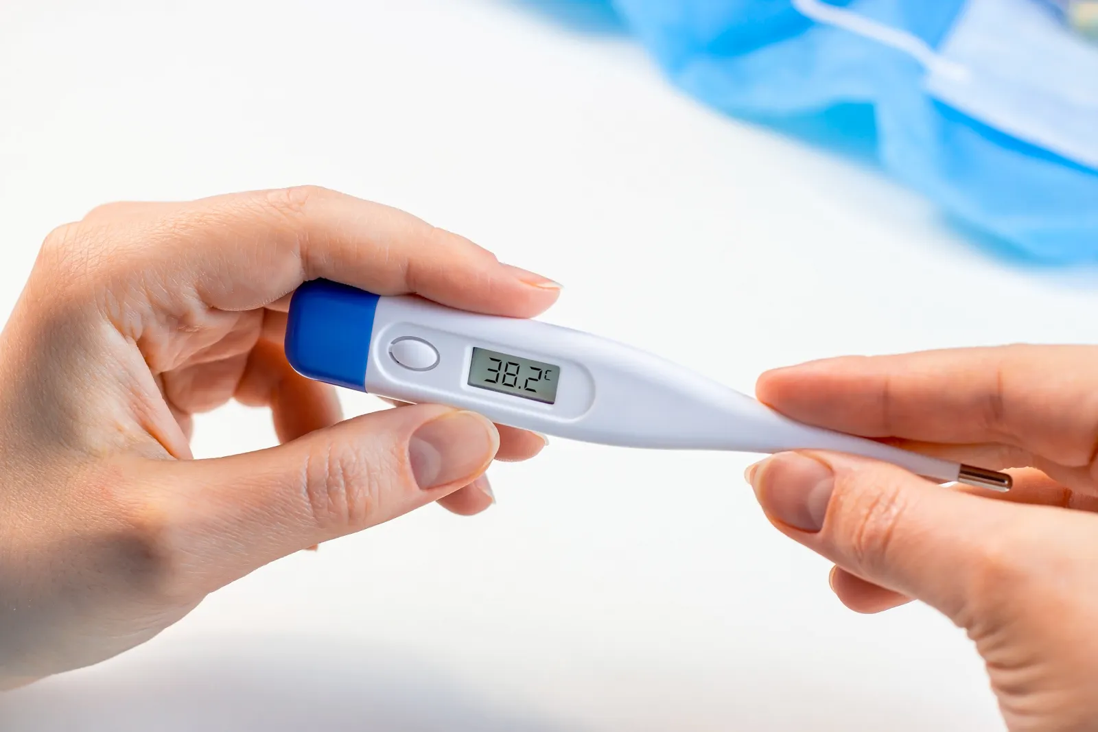 Woman hands holding a medicine digital thermometer with high body temperature measurement on light background.