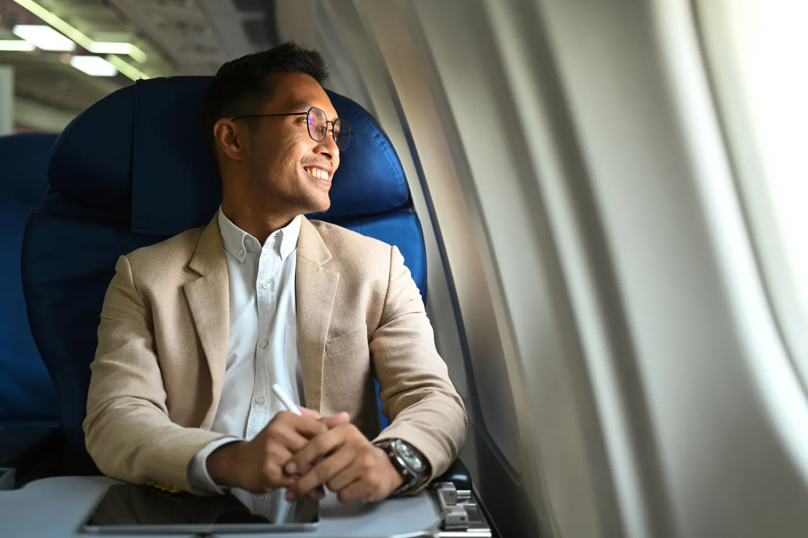 Man in a suit smiling while looking out the window of a plane.