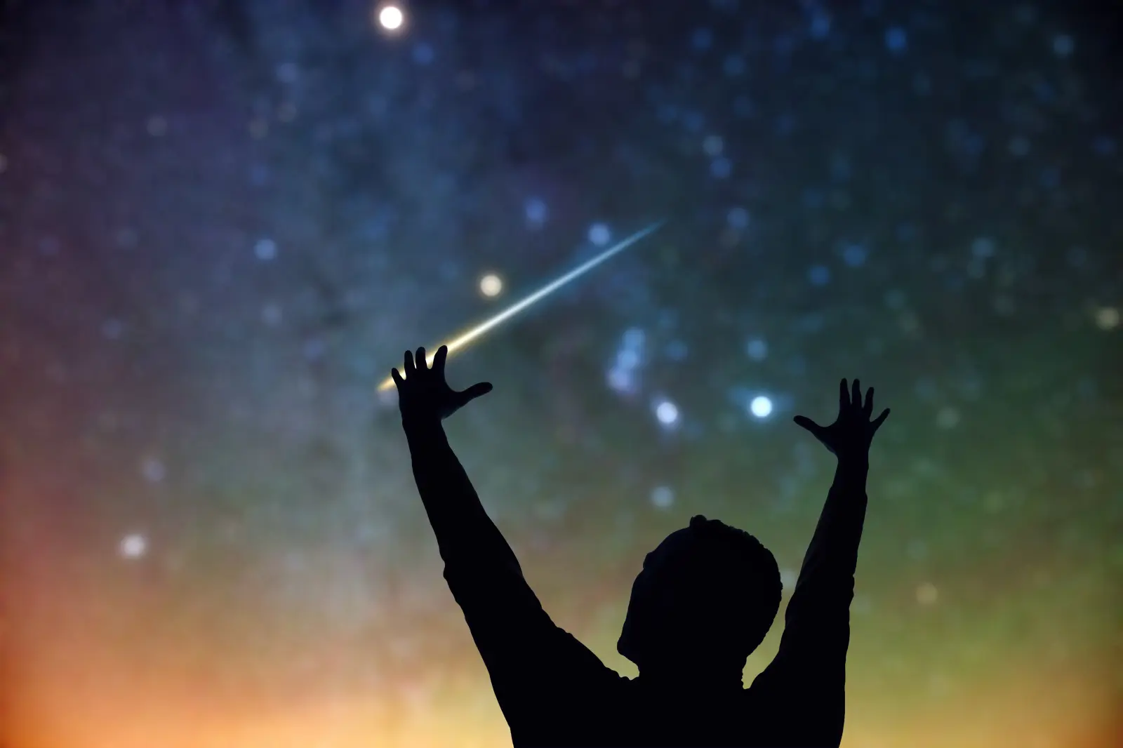 Silhouette of a man watching meteor shower in night sky with arms up.