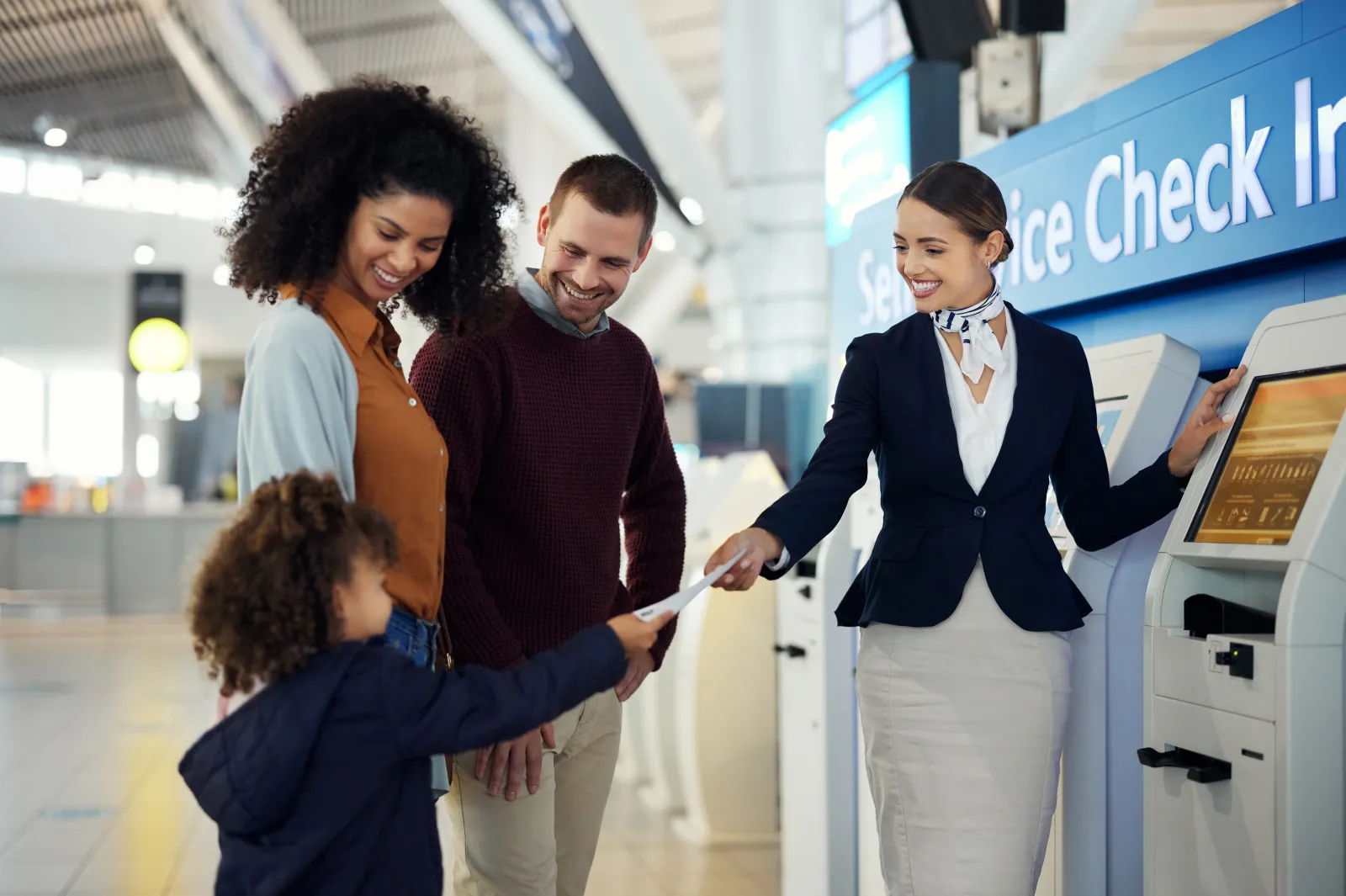 Airline worker assisting couple and child at check-in kiosk.