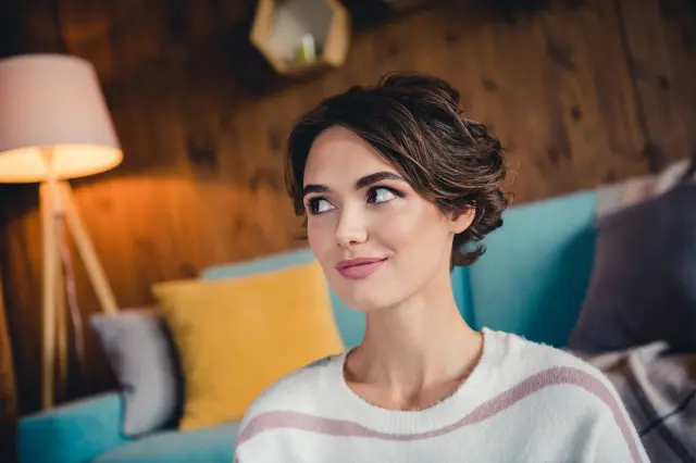 A stock image of a woman appearing pensive while looking up in a living room setting.