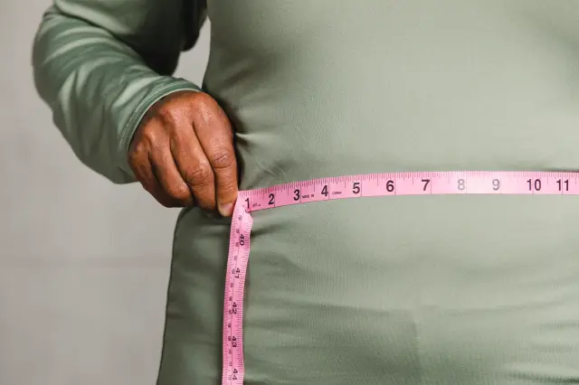 A man measures his waist with a tape.