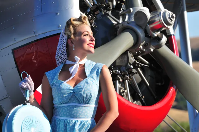 A woman dressed in 1940s src clothing near a plane.