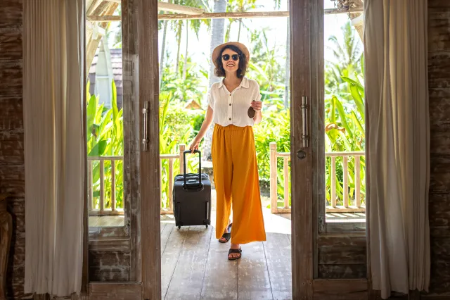 Woman rolling a suitcase into a hotel room.