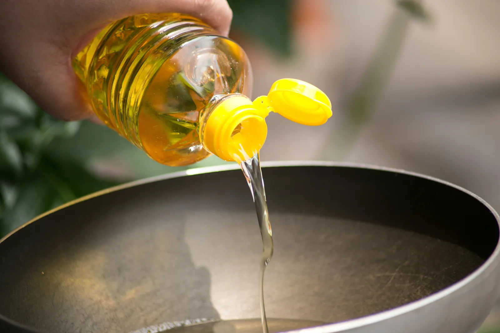 A person pours soybean oil into a hot pan for frying.