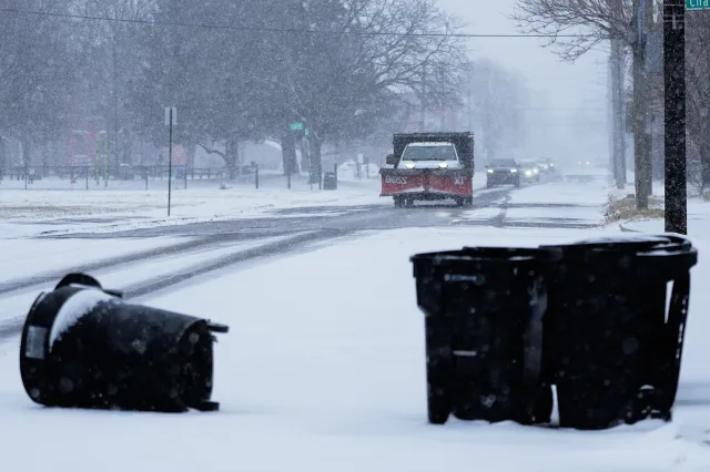 Turned over garbage cans are seen as a snowplow drives after a winter storm system hit South East Michigan, Monday, Dec. 29, 2025, in Detroit