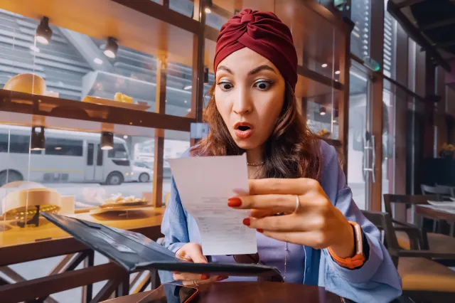 A woman appearing shocked while looking at the bill at a restaurant.