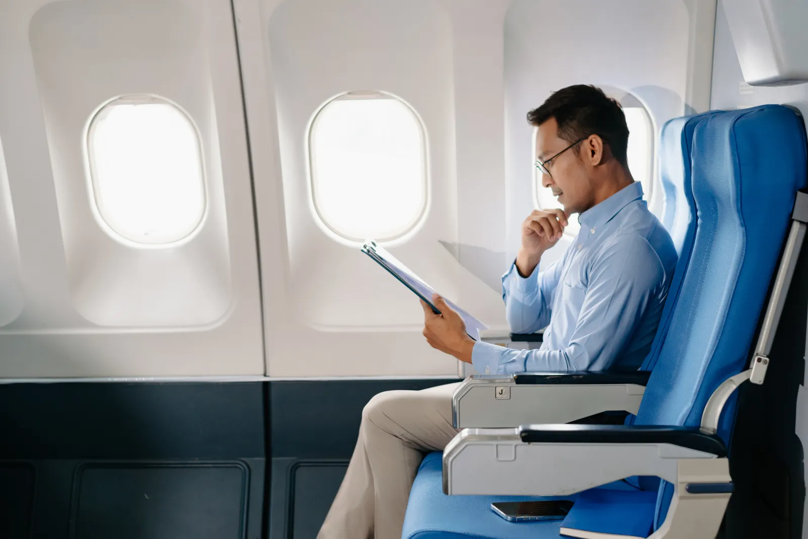 Man in window seat on plane, reading from clipboard.