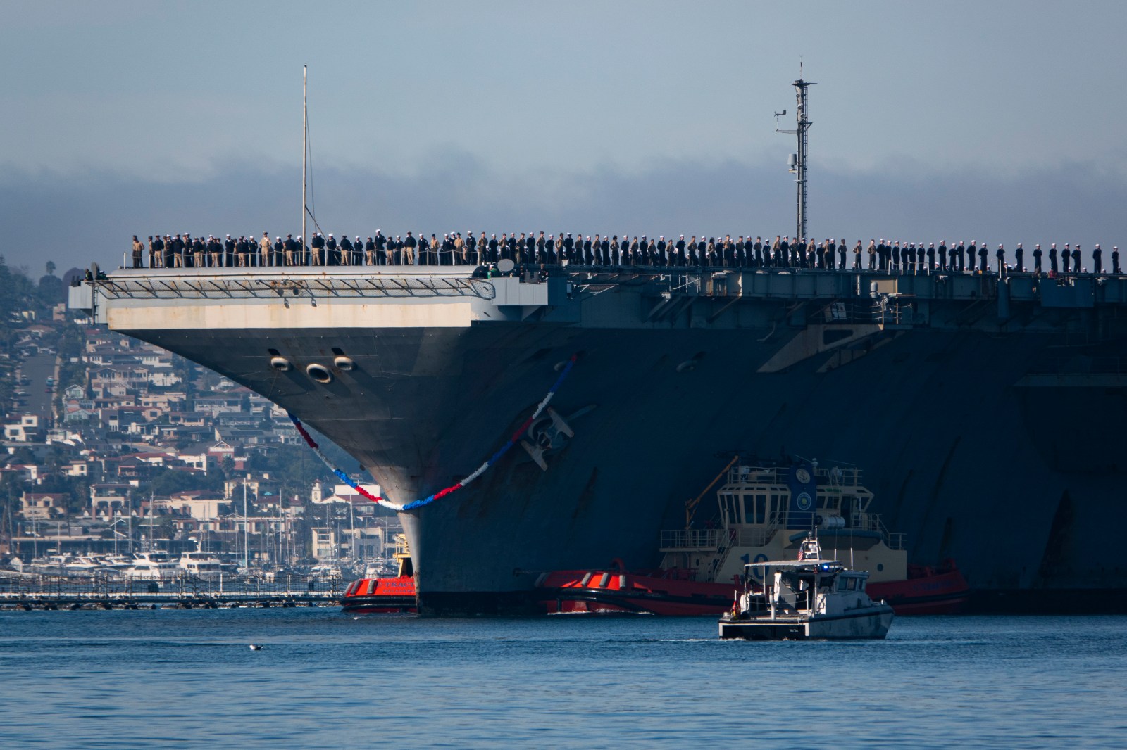 This image from December 20, 2024 shows a U.S. Navy Nimitz-class aircraft carrier USS Abraham Lincoln (CVN 72) is guided by tugboats in San Diego Bay,  California. 
