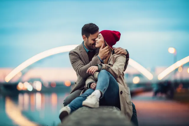 Couple sharing a tender moment while sitting on a stone wall by a river.