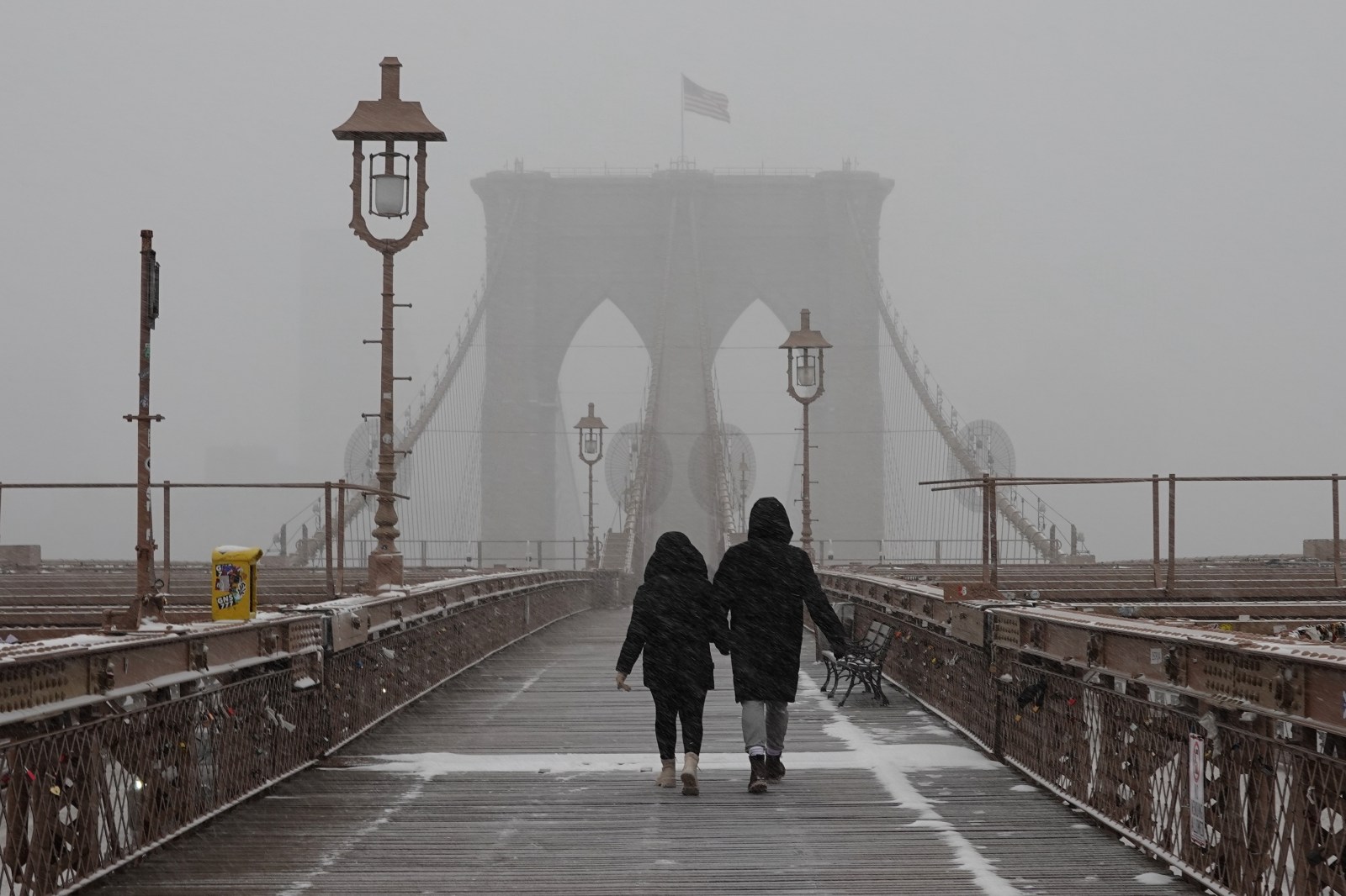 A couple holds hands as they walk across the Brooklyn Bridge as it snows on Sunday, Jan. 25, 2026, in New York. (AP Photo/Alyssa Goodman)