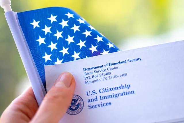 File image: Letter from USCIS and flag of USA in hand on green blurred background - stock photo