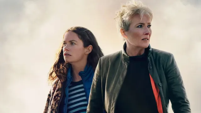 Two women stand in front of a cloudy sky looking in opposite directions
