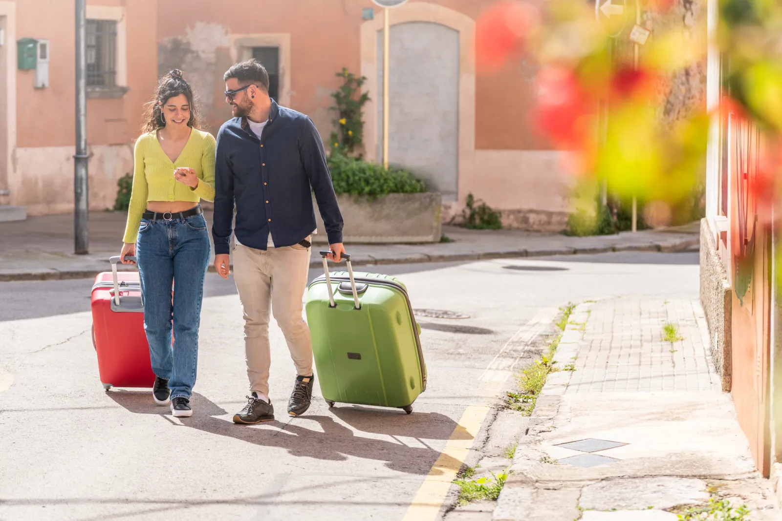 A tourist couple rolling their suitcases along a street.