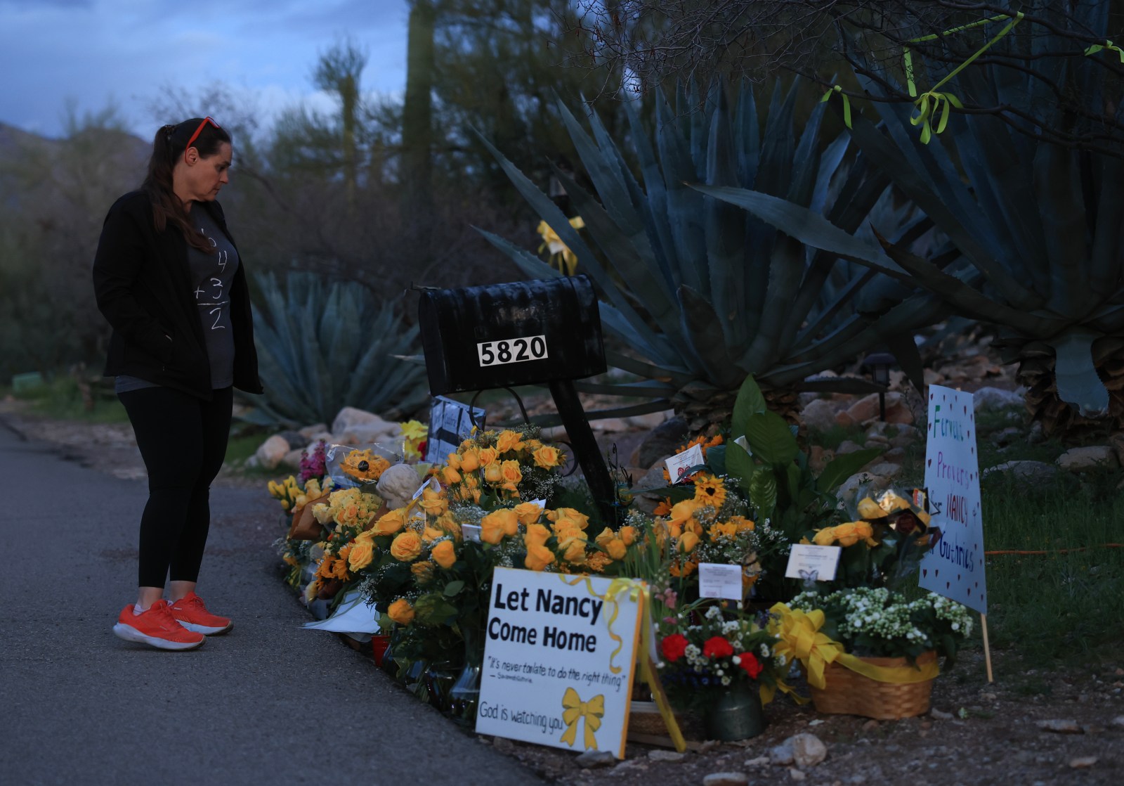 TUCSON, ARIZONA – FEBRUARY 18: Jeannie Maggard visits a memorial setup next to the driveway of the residence of Nancy Guthrie on February 18, 2026, in Tucson, Arizona. Law enforcement officials continue to search for Nancy Guthrie, the 84-year-old mother of U.S. journalist and television host Savannah Guthrie, after she went missing from her home on the morning of February 1st. (Photo by Joe Raedle/Getty Images)