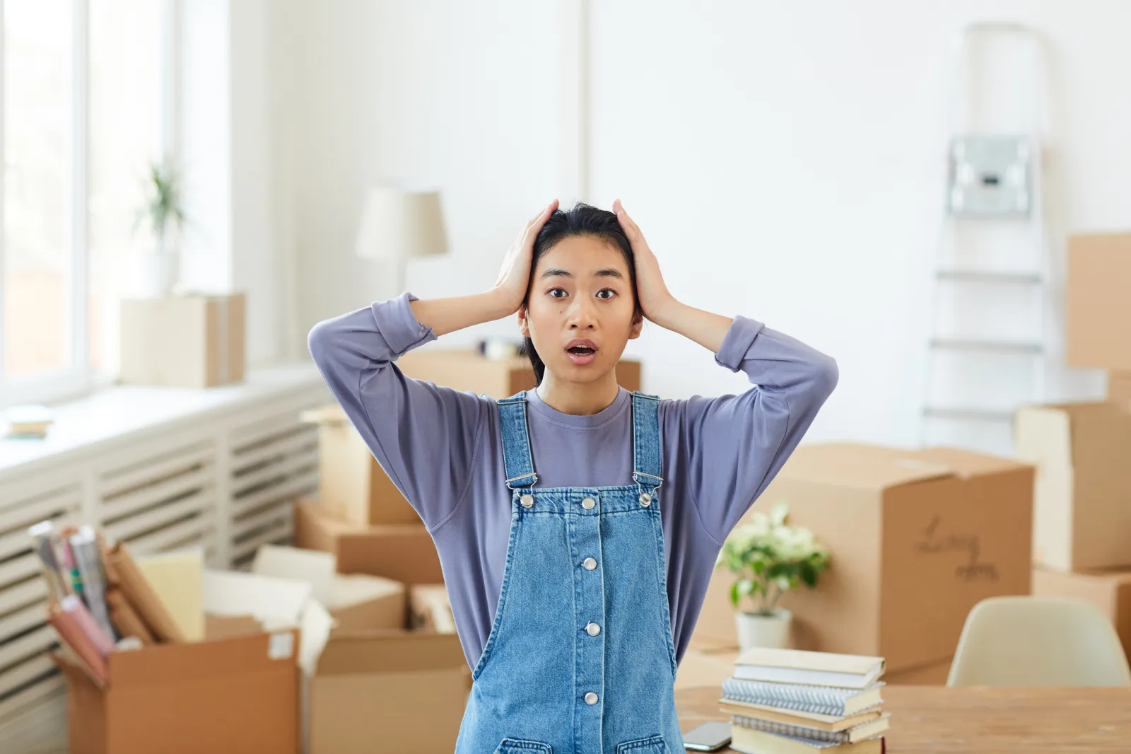 Woman shocked with hands on head while surrounded by moving boxes.