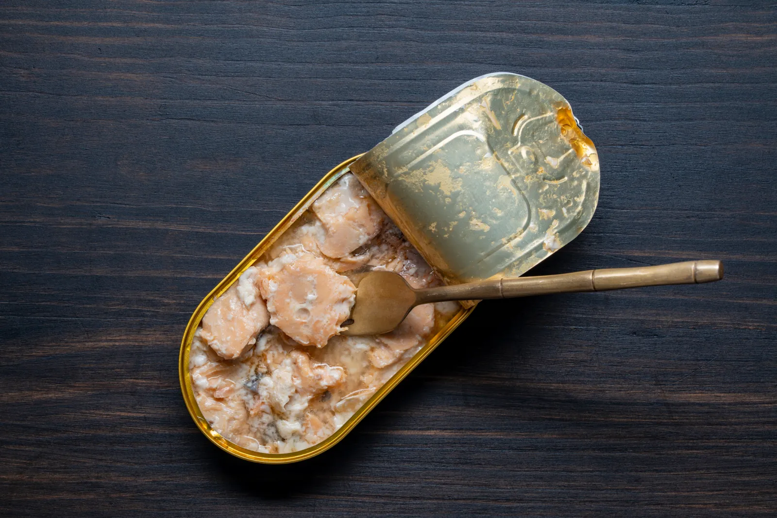 An opened tin can of salmon with a fork in it.