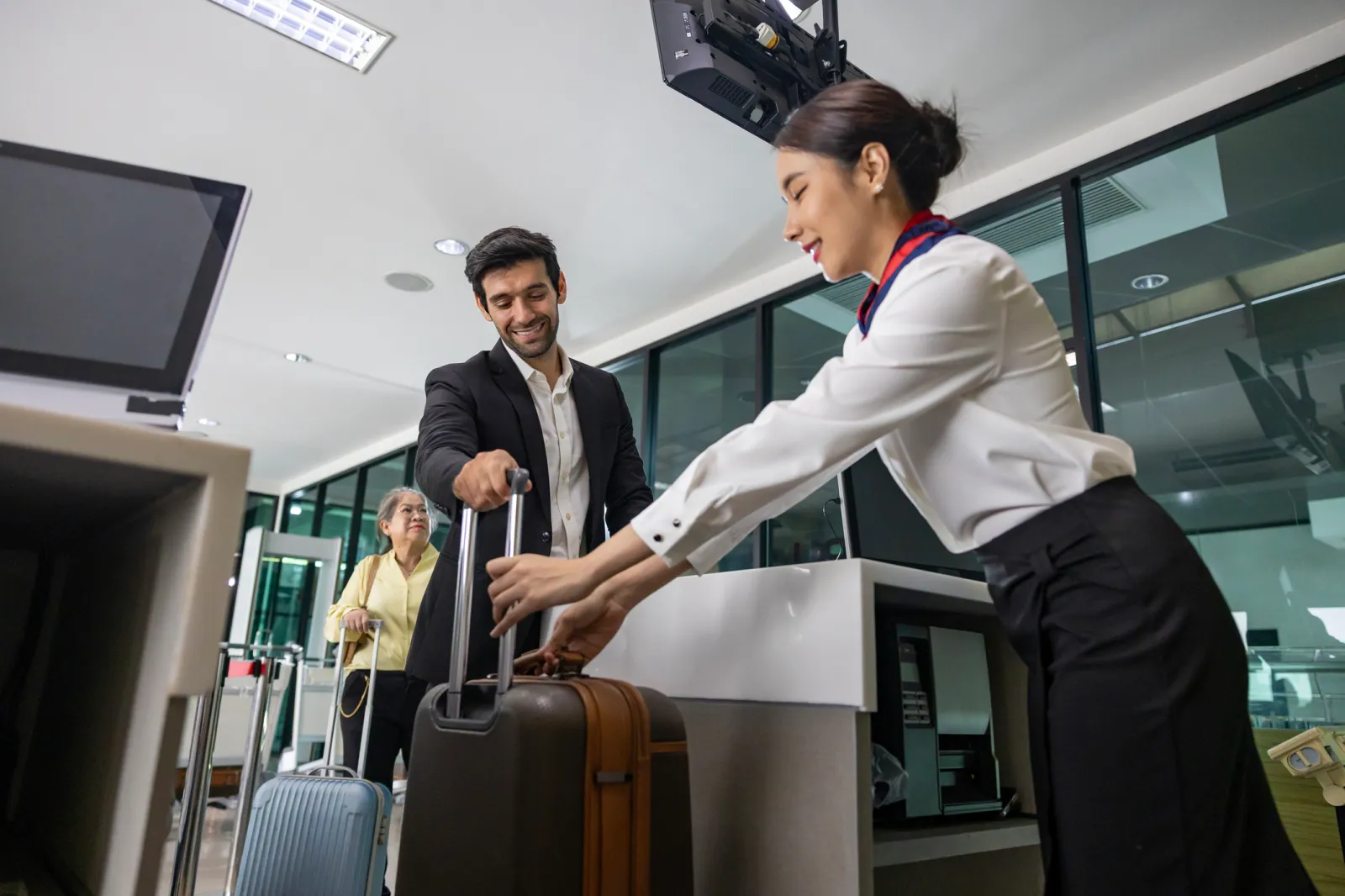 An airline worker helping passenger with suitcase at a check-in desk.