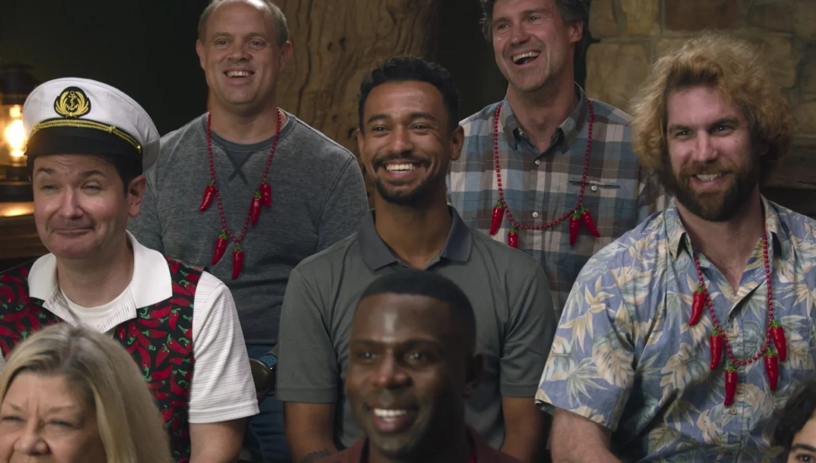 A group of people sitting down smiling, all of them are wearing necklaces of chili peppers.