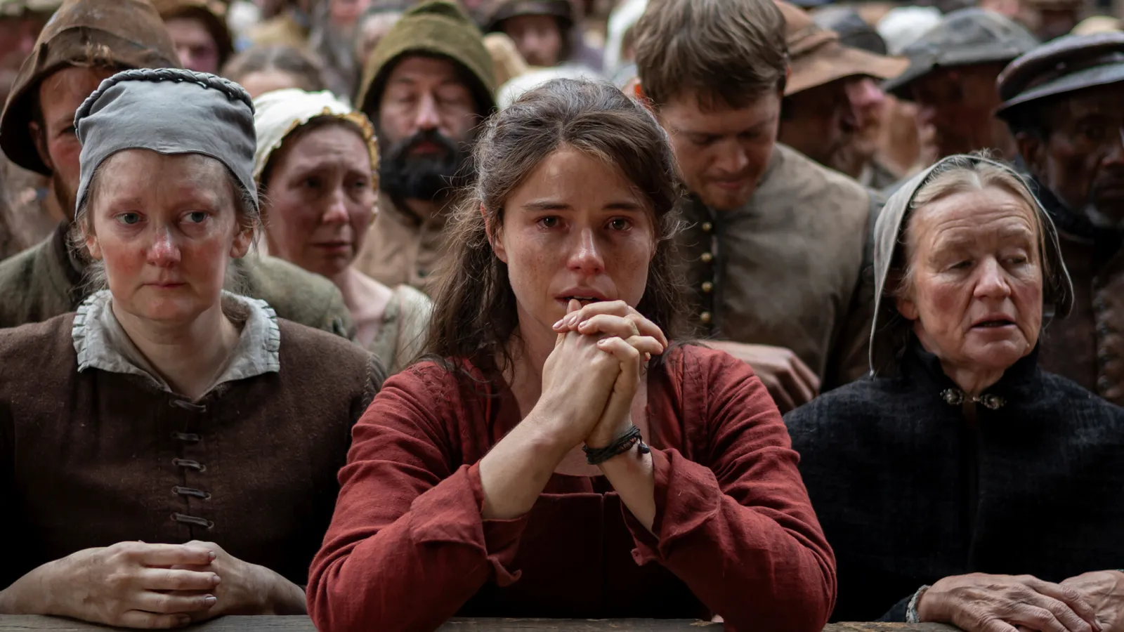 A woman in a red top cries in a crowd of peasants