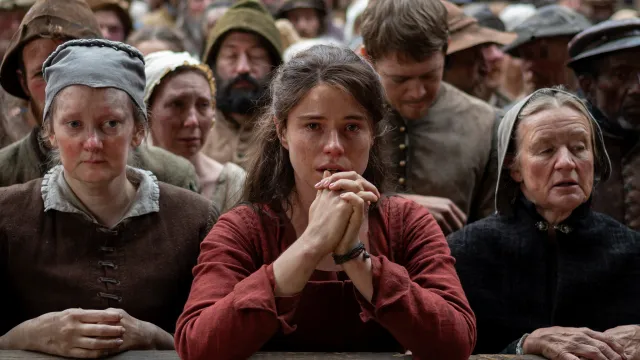 A woman in a red top cries in a crowd of peasants