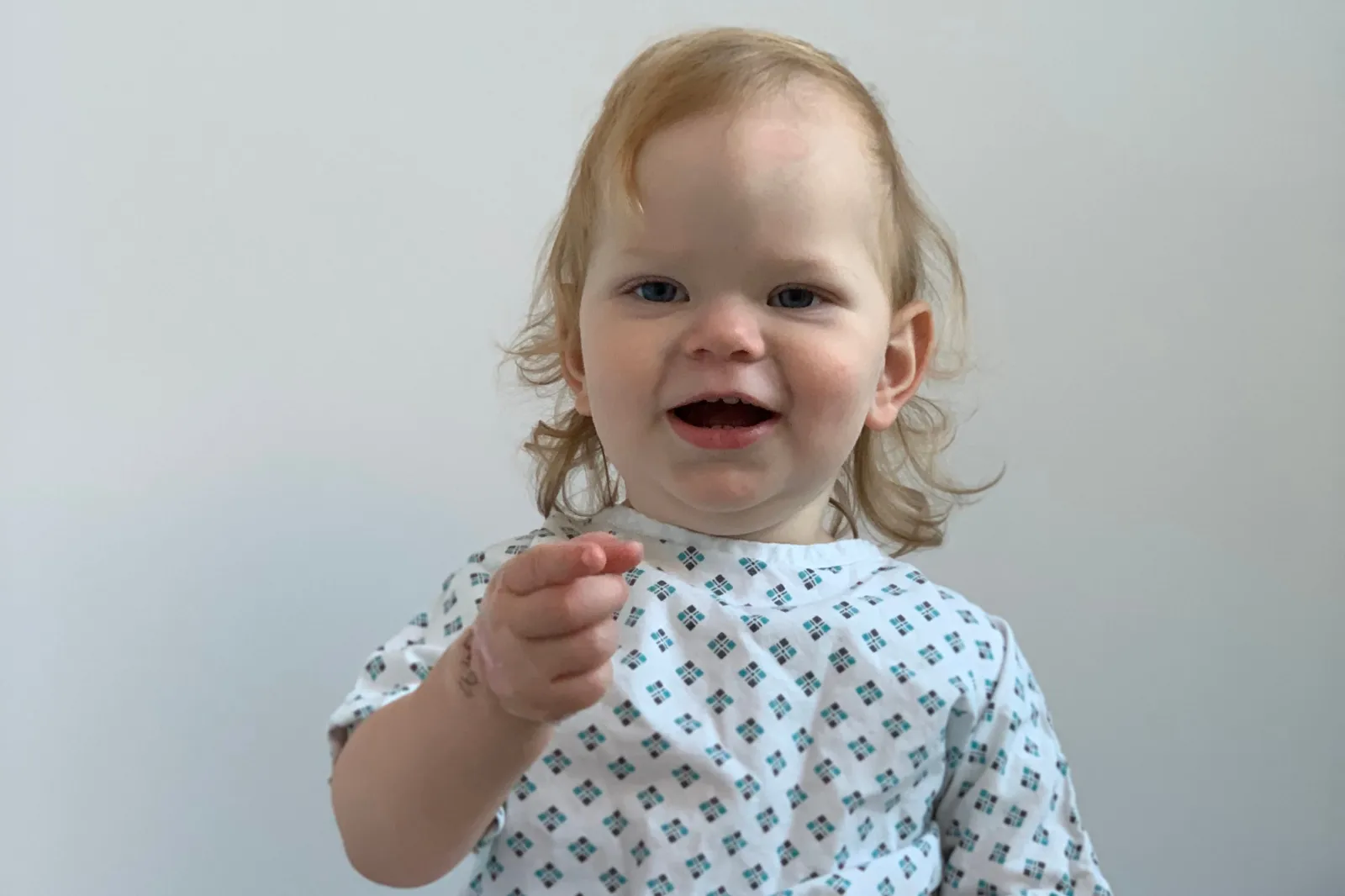 Hetty wearing a baby hospital gown pointing to the camera.