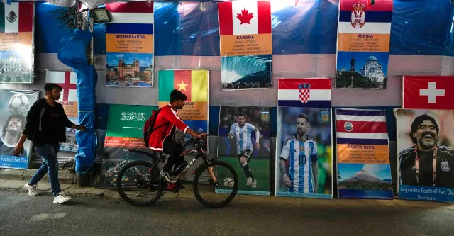 A youth pedals past a wall decorated with pictures of Diego Maradona and Lionel Messi and the flags of participating nations put up by fans to mark the soccer World Cup in Kolkata, India, on December 8, 2022.