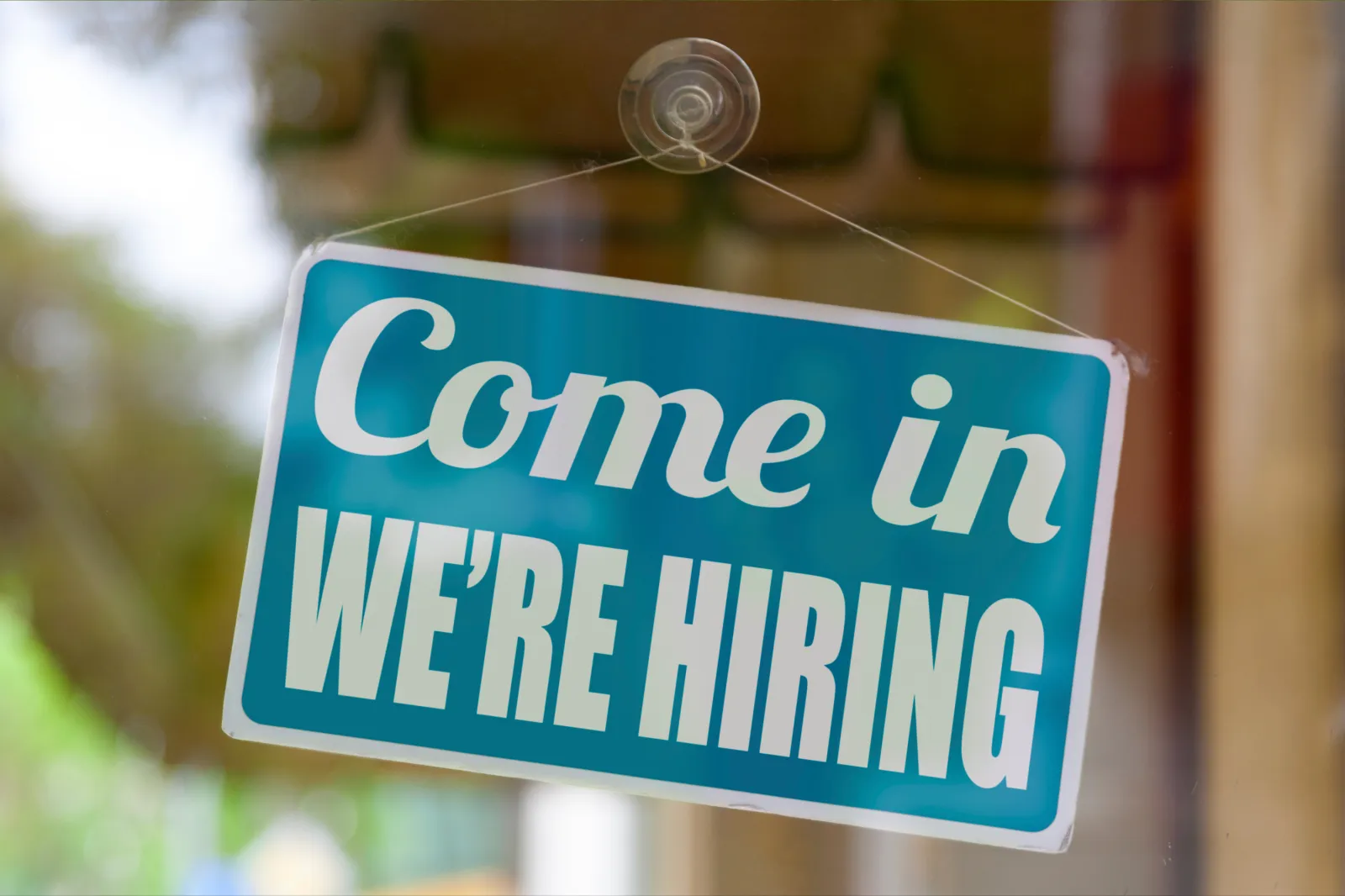 Stock image of a sign in a business window announcing the company is hiring.
