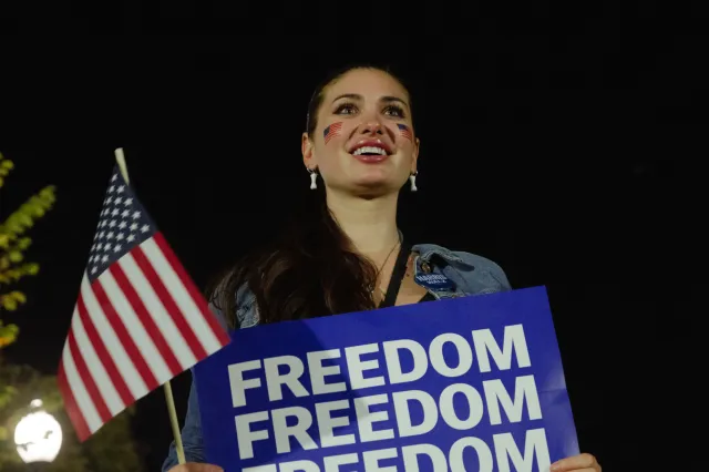 A young woman holds a symbolic American flag and a sign that says freedom in her other hand showing her support for US Vice President Kamala Harris, on the Ellipse of the White House in Washington, DC, US, on Tuesday, Oct. 29, 2024.