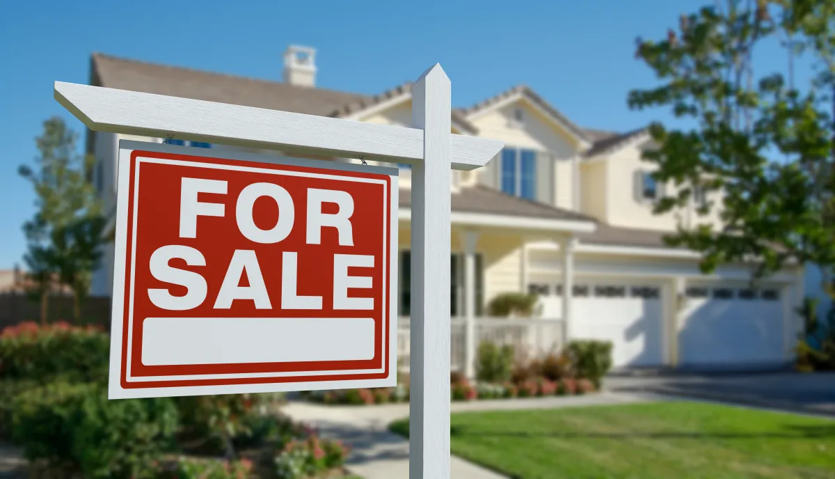 Stock image of a For Sale sign outside a large home.