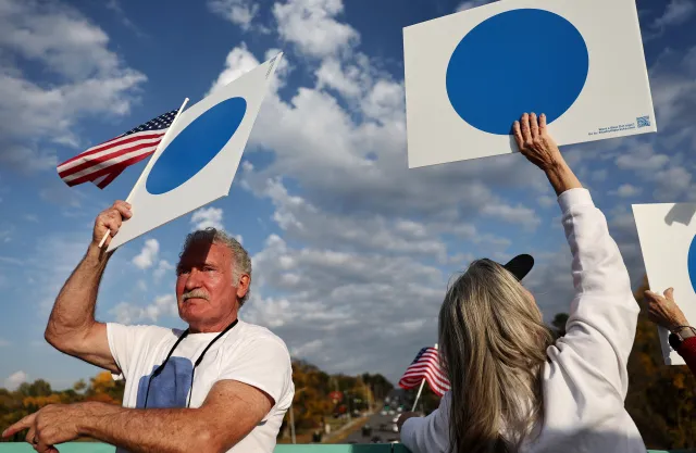 Demonstrators wave "Blue Dot" signs from a pedestrian bridge over rush hour traffic on October 24, 2024, in Omaha, Nebraska.
