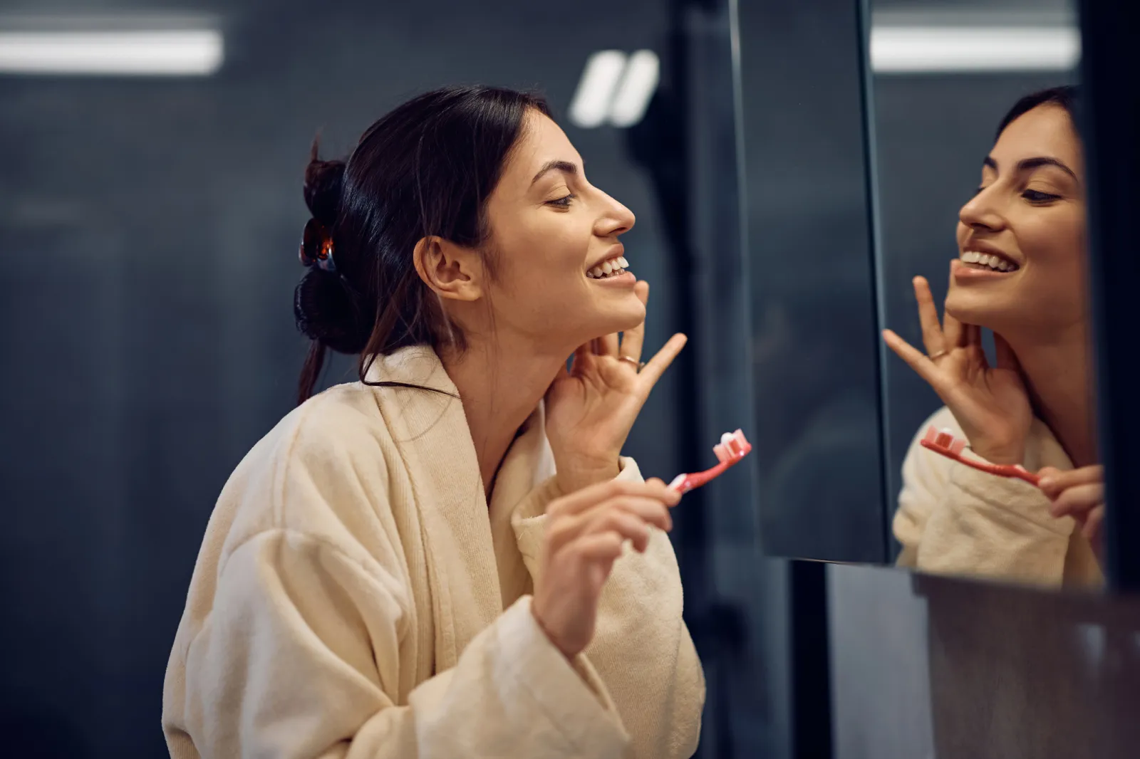 A stock photo of a woman checking her teeth in the mirror.