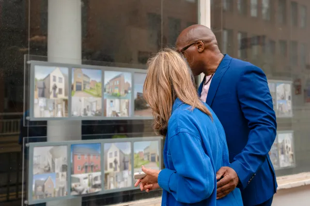 Stock photo: A couple looks at property listings displayed in a window.