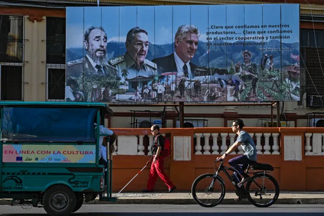 People pass near a poster of (L-R) Cuban late leader Fidel Castro, former President Raúl Castro and President Miguel Díaz-Canel in Havana, on May 20, 2026.