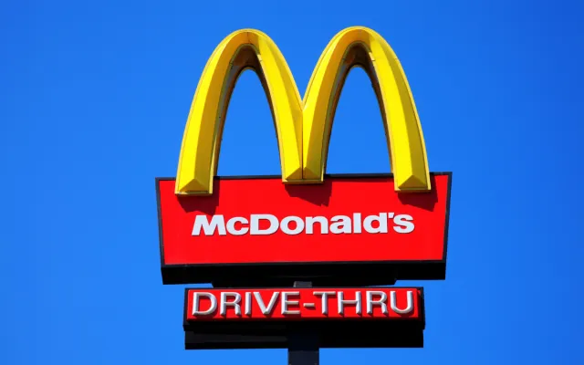 McDonald's yellow and red drive-thru logo advertising sign placed on a pole with a clear blue sky