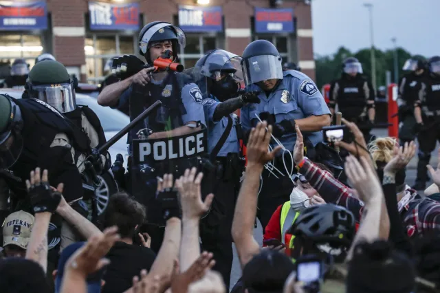 A police officer points a hand cannon at protesters who have been detained pending arrest on South Washington Street in Minneapolis, May 31, 2020, as protests continued following the death of George Floyd.