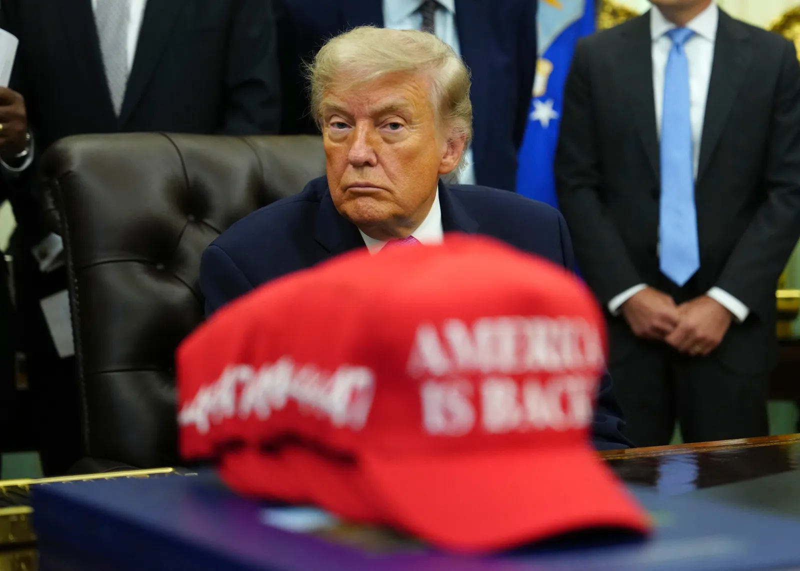 President Donald Trump sits in the Oval Office of the White House alongside a stack of red caps stating "America is Back" on June 26 in Washington. (AP Photo/Julia Demaree Nikhinson)