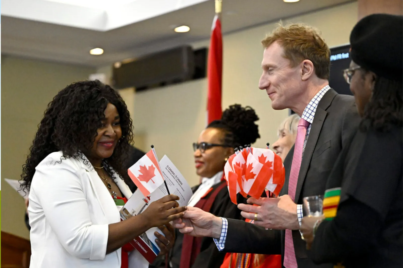 Cladice Awatia Tsafack receives a Canadian flag from Minister of Immigration, Refugees and Citizenship Marc Miller, left, after becoming a Canadian citizen during a citizenship ceremony in Ottawa, on Wednesday, Feb. 28, 2024.