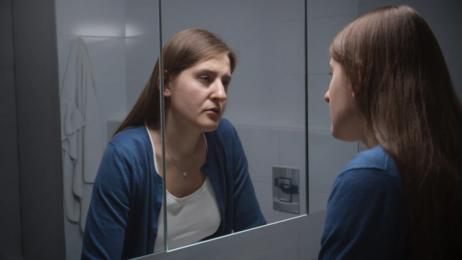 A stock image of an woman standing at sink and looking at her reflection.