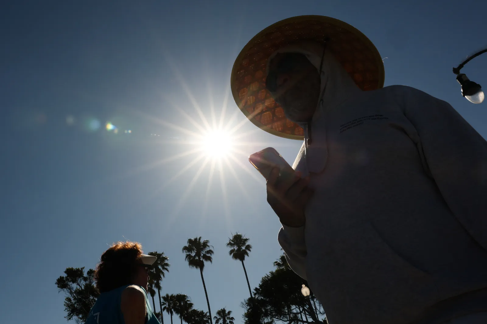 A person wears a hat for shade under the morning sun while walking along the Strand in Redondo Beach, California, on March 20 during a heat wave.