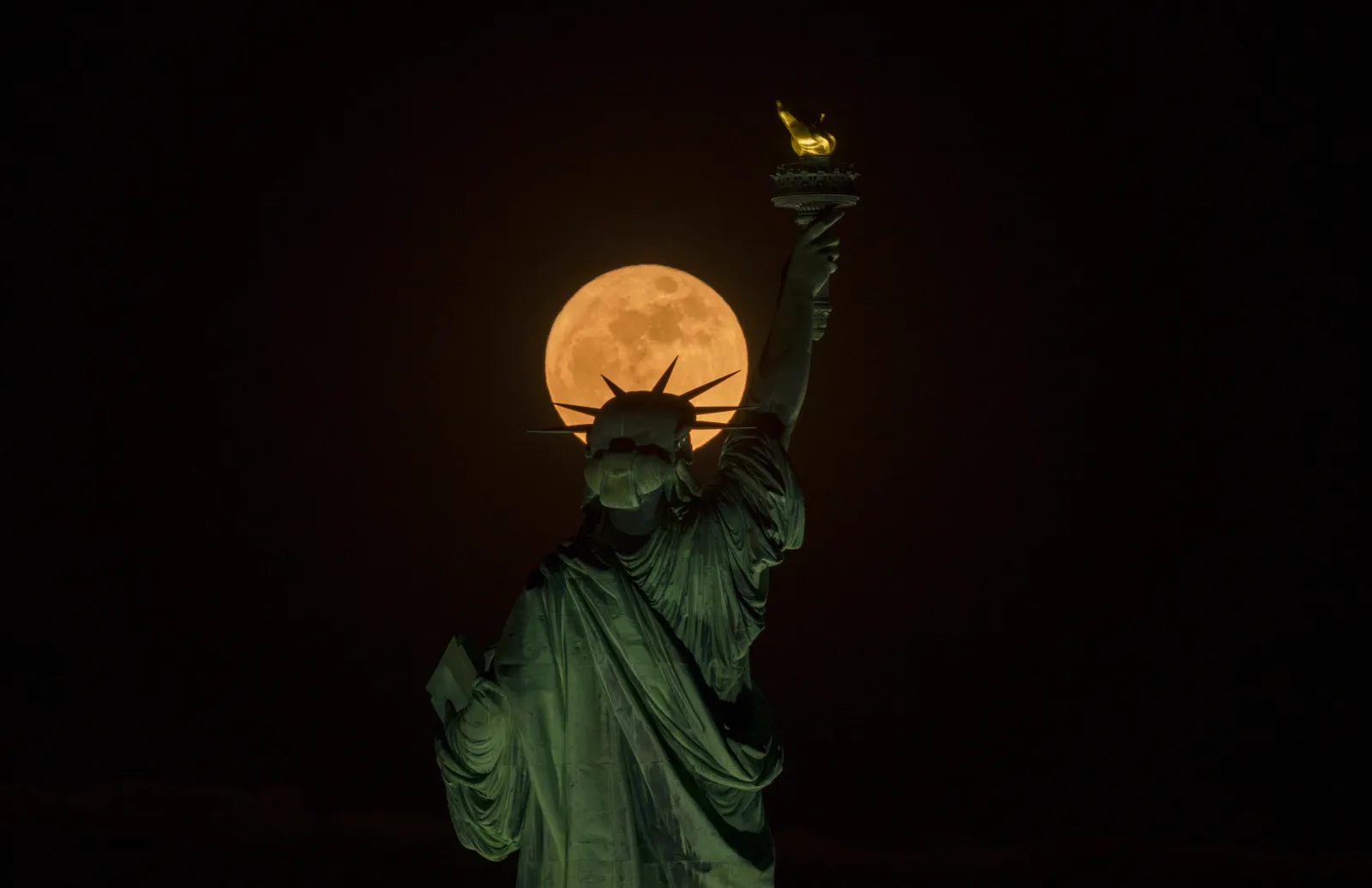The full Flower Moon rises behind the Statue of Liberty in New York City on May 1, 2026, as seen from Jersey City, New Jersey.