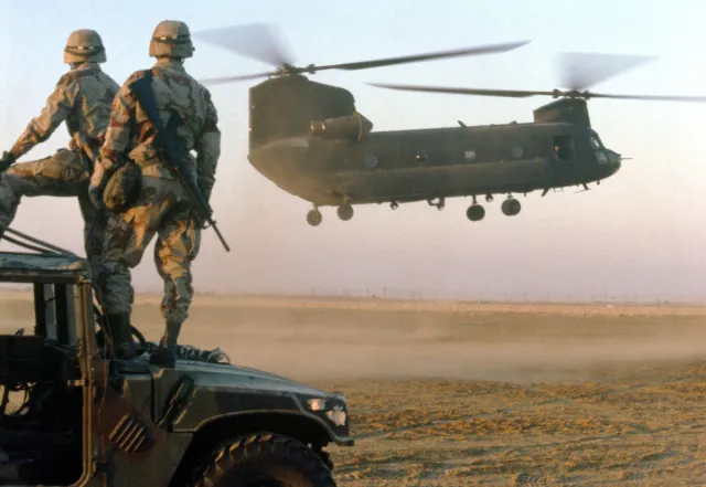 Soldiers of the 82nd Airborne Division stand atop an M-998 high-mobility multi-purpose wheeled vehicle as they watch a CH-47 Chinook helicopter prepare to touch down during Operation Desert Shield in 1990.