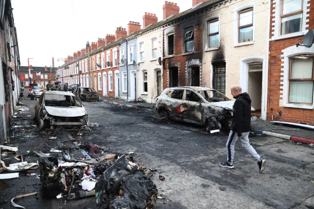 A man walks down a street with burned-out cars and houses in east Belfast, Northern Ireland, on Wednesday, June 10, 2026.