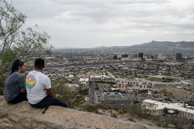 A man and woman sit on a ledge overlooking downtown on July 1, 2020, in El Paso, Texas.