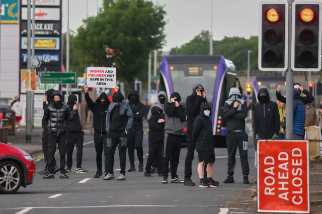Masked protesters gather on a road in north Belfast on Tuesday, June 9, 2026.