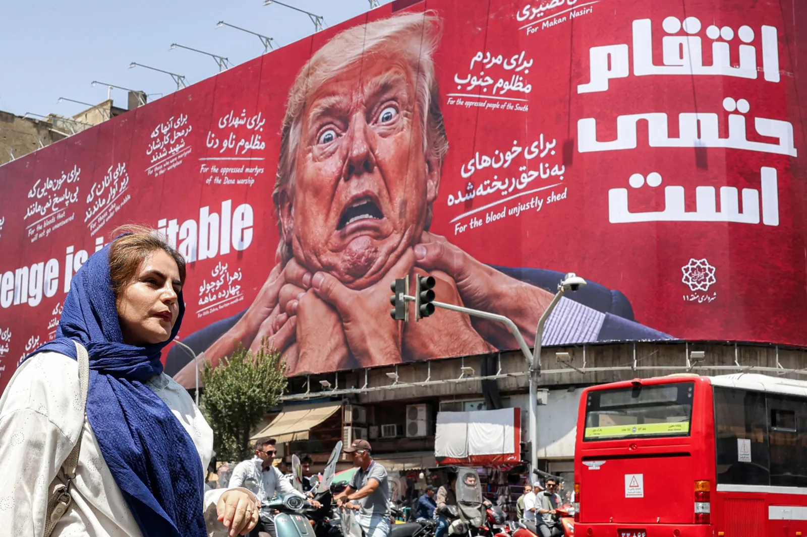 A woman walks past a large billboard pledging revenge against US President Donald Trump along Jomhouri Street in central Tehran on July 27, 2026.